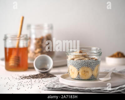 Gesundes Frühstück Konzept und Idee - chia Pudding mit organischen Banane und Biene Blütenstaub. Glas Glas Chia puding auf weißem Marmortisch. Kopieren Sie Platz für Text Stockfoto