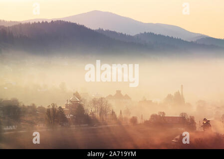 Misty sunrise Szene in einem ländlichen Dorf in den Karpaten, in der Ukraine. Fokus auf Kirche Stockfoto