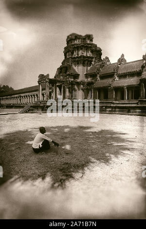 Kambodscha, Angkor Wat; 02/28/2016: Eine Frau sitzt im Schatten einer Palme im Innenhof auf der linken Seite der Eingang zum Angkor Wat. Stockfoto