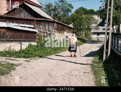 Lokale Maramures ältere Dame zu Fuß auf der Straße in Richtung der Markt mit einem Korb auf dem Rücken Breb, Rumänien Stockfoto