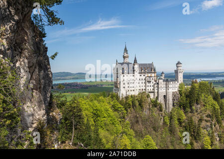 Schloss Neuschwanstein in Deutschland von Süden mit einem Felsen auf der linken Seite in Bild und blauer Himmel und See forgensee im Hintergrund. Stockfoto