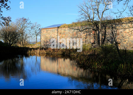 Kleiner Teich mit Reflexionen auf den blauen Himmel und Befestigungsanlagen in Piper's Park, Suomenlinna, die zum UNESCO-Weltkulturerbe in Helsinki, Finnland. Okt 2019 Stockfoto