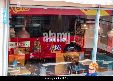 Edinburgh, Großbritannien - 5. Juli 2019: Schaufenster Reflexion eines roten Hop-on Hop-off City Sightseeing Tour bus und ein Passant in Edinburgh City Stockfoto