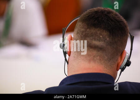 Flache Tiefenschärfe (selektive Fokus) Bild mit einem Mann auf einem Stuhl sitzen und zuhören zu einer Konferenz und Kopfhörer mit Übersetzung auf h Stockfoto