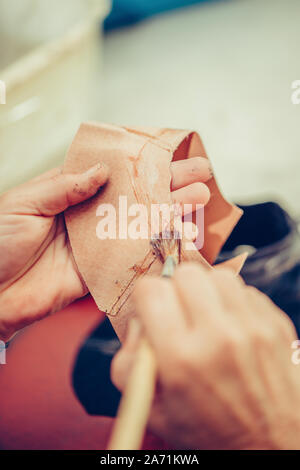 Die Hände eines erfahrenen Arbeiter in den handgefertigten Schuhindustrie, alleinige kleben Aufgaben, Leim auf die Teile der Schuh. Stockfoto