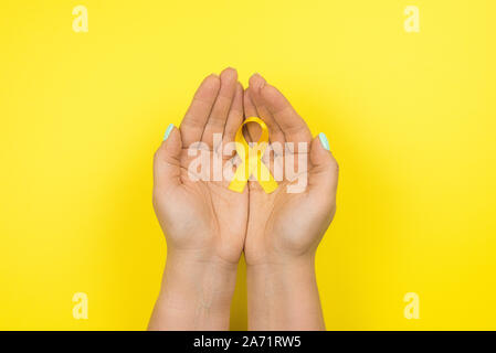 Gelb Gold Ribbon in den Händen eines Mädchens auf einem gelben Hintergrund. Kinder Krebs Konzept. Sstsein Monat. Krebs im Kindesalter Tag Februar, 15. Stockfoto