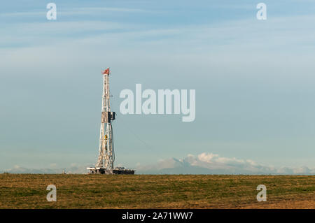 Bohrinsel Derrick fangen die Sonne am Ende des Herbstes mit den Rocky Mountains im Hintergrund Stockfoto