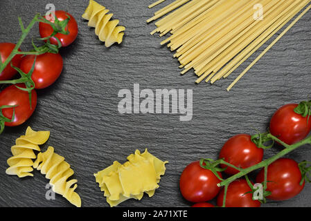 Hintergrund und Rahmen mit Textfeld verschiedener Pasta wie Spaghetti und spiralförmige Nudeln mit frischen Tomaten auf einer Schiefertafel Teller gemacht Stockfoto