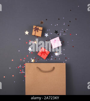 Kraftpapiersack auf hellen dunklen Hintergrund. Mit Geschenkboxen und Konfetti. Schwarzer Freitag Weihnachtsgeschenk Vorbereitung Konzept. Stockfoto