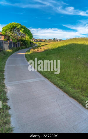 Konkrete weg auf einem Gras bedeckten Hügel unter blauem Himmel an einem sonnigen Tag Stockfoto