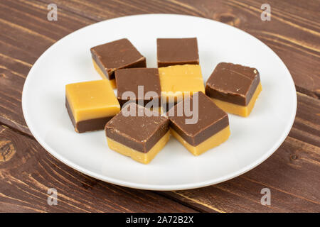 Gruppe der Acht ganze süsse braune Karamell Schokolade Süßigkeiten auf weißer Keramik Platte auf braunem Holz Stockfoto