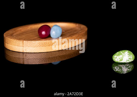 Gruppe von drei ganzen jelly bean Candy auf runden Bambus Untersetzer auf schwarzem Glas isoliert Stockfoto