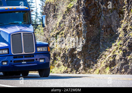 Classic Big Rig professionelle Industrial Grade American Motorhaube blau Transport Semi Truck bei laufendem Traktor auf kurvigen Bergstrasse mit Felswand o Stockfoto