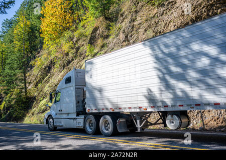 Big Rig classic Weiß pro Amerikanische Motorhaube Semi Truck mit vertikalen Auspuffrohre Transport gefroren Cargo in gekühlten Auflieger, die auf dem Stockfoto