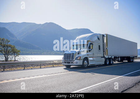 Professionelle Big Rig Semi Truck mit Chrom Zubehör Transport gefroren Cargo in gekühlten Auflieger bewegen auf der Straße entlang des Flusses wi Stockfoto