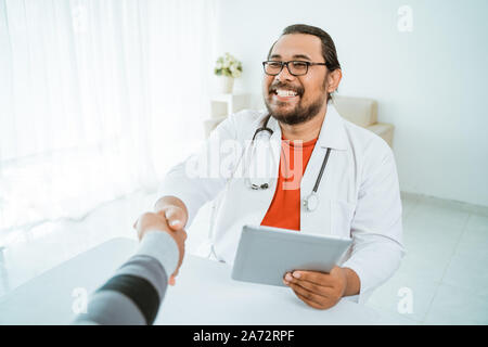 Lächelnd Arzt zitternden Hand mit Patienten in seinem Büro Stockfoto