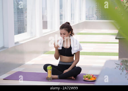 Junge Frau in Sportkleidung sitzen auf Wand an Dach bauen und sie ihr Smartphone Stockfoto