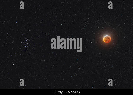 Der Mond in der Mitte total eclipse, am 20. Januar 2019, mit der es scheint neben den Bienenstock star Cluster, Messier 44, in Krebs. Dies war der einzigartige Blick Stockfoto