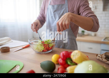 Nahaufnahme des Menschen mischen Salat mit Salat und Pfeffer in der Schüssel Stockfoto