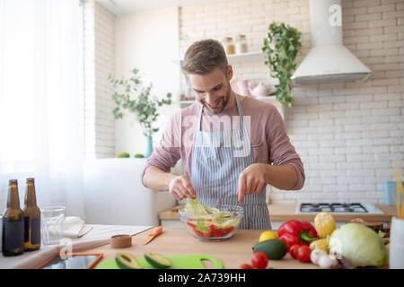 Fröhlicher Mann kochen Salat mit Salat und Gemüse Stockfoto