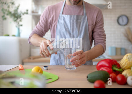 Mann mit Schürze gießt Wasser in Glas Stockfoto
