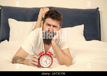 Hipster bärtiger Mann im Bett lagen mit Wecker. Zeit aufzuwachen. Warum sollten Sie früh aufstehen jeden Morgen. Nutzen für die Gesundheit der Früh aufstehen. Aufwachen frühzeitig, mehr Zeit für die Vorbereitung und zeitgerecht erfolgen. Stockfoto