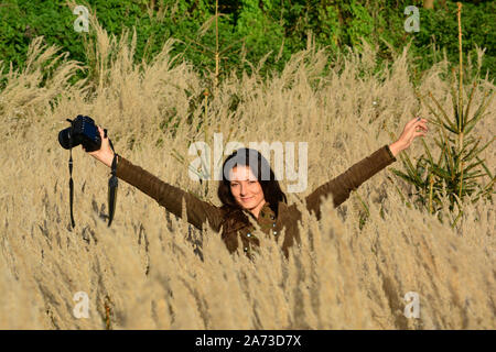 Junge Langhaarige brunette Mädchen, Natur Fotograf in hohen, golden farbiges Gras in der Mitte des Herbstes Feld, auf der Suche nach heiteren gut getan Job Stockfoto