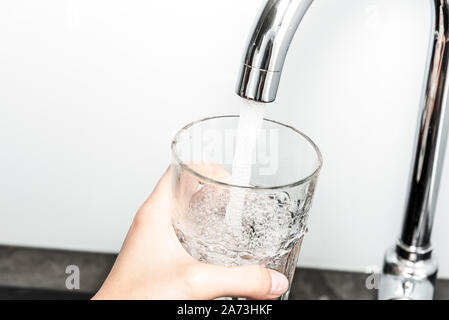 Weibliche hand Füllung Glas mit Wasser aus dem Wasserhahn in der Küche in Nahaufnahme. Stockfoto