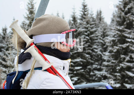 Junge, hübsche Mädchen in weißen Skianzug, mit grauer Kappe, googgles und Skistöcke mit Seilbahn, Skigebiet Kopaonik, Serbien Stockfoto