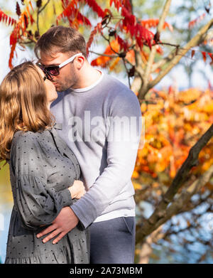 Romantische junge Paar küssen draußen im Park unter bunten Herbst Bäume mit roten und orangefarbenen Laub Stockfoto