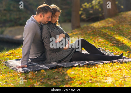 Liebe Paar mit schwangeren Frau zusammen auf eine Wolldecke im Park Verklebung mit ihrem ungeborenen Baby Stockfoto