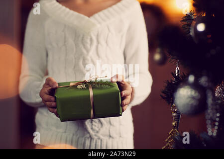 Nahaufnahme der Frau in weißen Pullover in der Nähe der Weihnachtsbaum und Holding Weihnachten in ihre Hände vorhanden Stockfoto