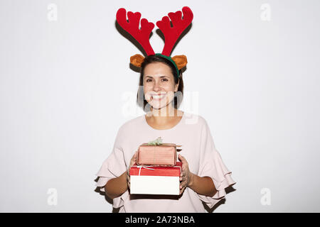 Portrait von Frau sucht sich Hörner von Hirsch holding Weihnachtsgeschenke und lächelnd an der Kamera auf weißem Hintergrund Stockfoto