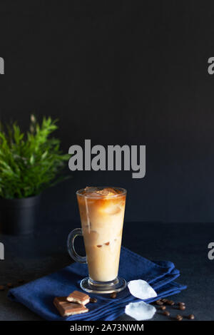 Eiskaffee in ein hohes Glas mit Sahne auf schwarzem Hintergrund. Kalter Kaffee mit Würfeln aus Eis und Sahne. Stockfoto