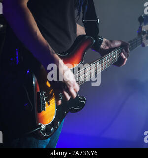 Gitarrist spielt E-Bass Gitarre auf eine dunkle Bühne, bis square Foto mit weichen selektiven Fokus nah, live Musik Thema Stockfoto