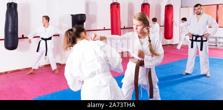 Portrait von sportlichen Kinder im Paar Beherrschung neuer Karate bewegt sich während der Gruppe Klasse mit männlichen Trainer Stockfoto