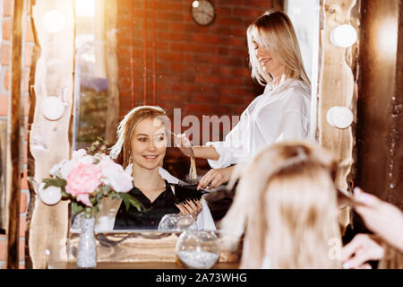 Haarpflege im modernen Spa Salon. Junge attraktive Frau mit niedlichen Lächeln über sich selbst im Spiegel an Beauty Salon suchen, zufrieden mit der Arbeit der professionellen h Stockfoto