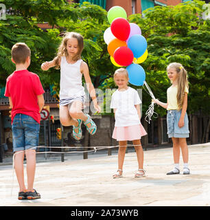 Mädchen Überspringen auf chinesische Seilspringen mit Freunden und einer der Freunde holding Ballons Stockfoto