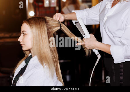 Professionelle female Friseur, Stylist, Frisur zu schönen blonden Client und Haarglätter in einem Schönheitssalon. Haare schneiden, Haarpflege anhand von quantitativen Simulatio Stockfoto