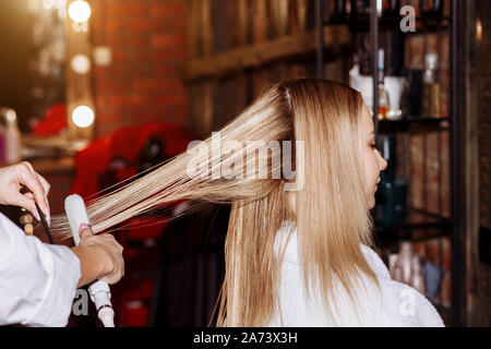 Professionelle female Friseur, Stylist, Frisur zu schönen blonden Client und Haarglätter in einem Schönheitssalon. Haare schneiden, Haarpflege anhand von quantitativen Simulatio Stockfoto