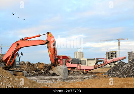 Schwerer Raupenbagger last Stein, mit alten Asphalt oder Beton Abfall in eine Mobile Backenbrecher Maschine. Die Zerkleinerung und Verarbeitung in Kies für Recycling Stockfoto