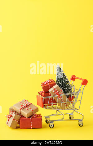Warenkorb voll von verschiedenen Geschenkboxen und ein Weihnachtsbaum auf gelben Hintergrund. Weihnachten Verkauf Konzept. Stockfoto
