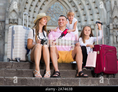 Glückliche Eltern mit Kindern sitzen auf alten Kathedrale Schritte suchen Karte Stockfoto