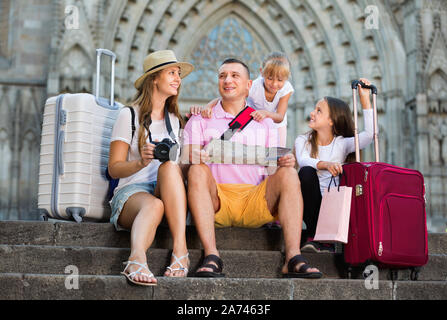 Positive lächelnde Familie von Touristen auf Treppen lesen Karte auf Papier Stockfoto