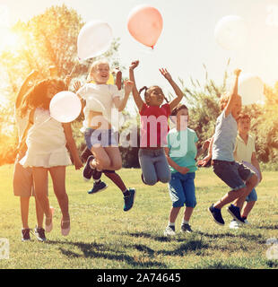 Gruppe der glückliche Kinder holding Ballons und gemeinsam springen in Park Stockfoto