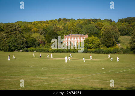 Ein Cricketspiel in Hambleden, Buckinghamshire, mit dem Haus Kenricks, das 1725 erbaut wurde Stockfoto