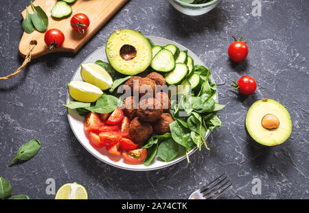 Salat mit Avocado, Falafel, Gurke, Cherry Tomaten und Spinat auf schwarzen Stein Hintergrund. Gesund vegan Mittagessen Schüssel Stockfoto