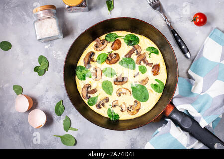 Omelette mit Pilzen und Spinat in eiserne Pfanne auf konkreten Hintergrund. Ansicht von oben Stockfoto