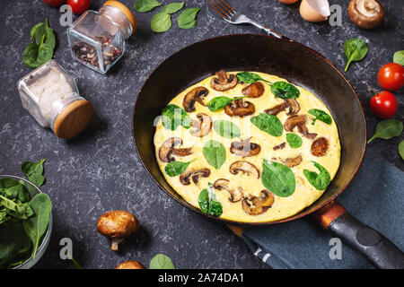 Omelette mit Pilzen und Spinat in eiserne Pfanne auf dem schwarzen Stein. Stockfoto