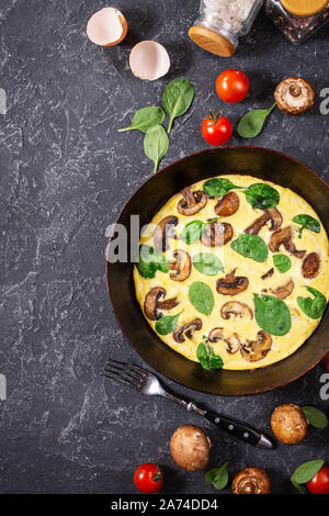 Omelette mit Pilzen und Spinat in eiserne Pfanne auf dem schwarzen Stein. Ansicht von oben Stockfoto